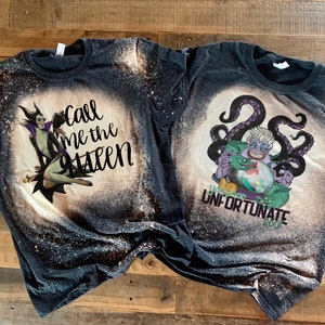 Op de afbeelding: Twee zwarte T-shirts met bleekdesigns met Disney-schurken. Het eerste shirt heeft een bleekdesign van Maleficent uit Doornroosje met de tekst "Call me the Queen". Het tweede shirt heeft een bleekdesign van Ursula uit De Kleine Zeemeermin met de tekst "You poor unfortunate soul".