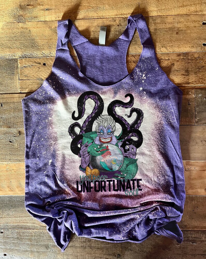 Op de afbeelding: Paarse tanktop met een ontwerp met bleekmiddelspatten met Ursula uit De Kleine Zeemeermin. Het ontwerp bevat Ursula's tentakels, een groene zeeslang en een kristallen bol. De tekst "You poor unfortunate soul" is onder de afbeelding gedrukt.