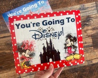 May include: A red and white jigsaw puzzle with a white background. The puzzle features Mickey and Minnie Mouse, Cinderella's castle, and the text "You're Going To Disney!"