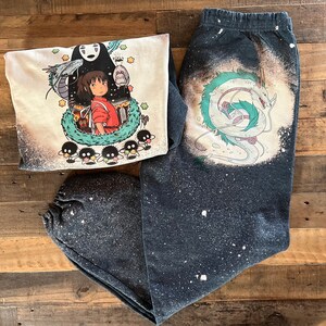 May include: A black and white graphic print of a dragon and a girl with a white background on a black and white sweatshirt. The sweatshirt has a distressed look with white splatter paint.