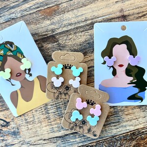 May include: Three sets of colorful Mickey Mouse-shaped earrings. Each set features two earrings in a different pastel color: light green, pink, and light blue.