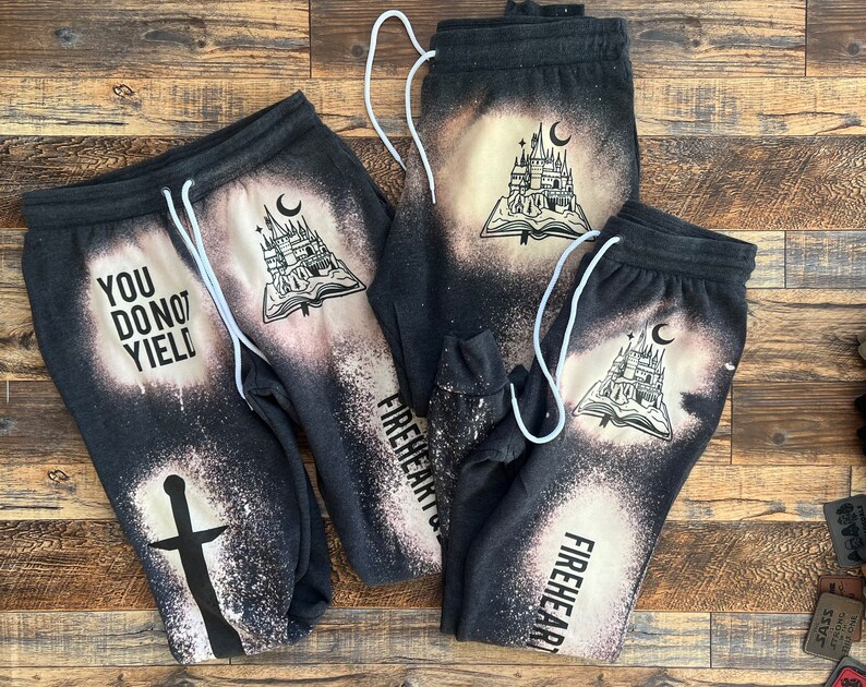 May include: Three pairs of black sweatpants with bleach-splattered designs. One pair features the text "You Do Not Yield" and a sword. The other two pairs feature a castle and book design and the text "Fireheart".