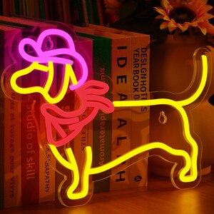 May include: A neon sign shaped like a dachshund wearing a pink hat. The sign is lit up and glowing yellow and pink.