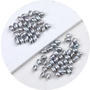 May include: A large group of oval-shaped, light grey pearls on a white surface. The pearls are scattered in two groups.