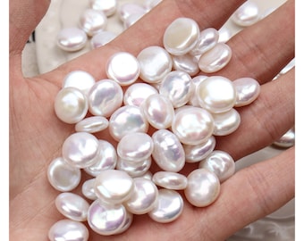 May include: A close-up of a hand holding a pile of white, round, smooth pearls. The pearls are of various sizes and have a slight iridescent sheen.
