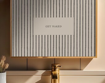 May include: A rectangular wall art piece in a gold frame featuring a vertical dark gray striped pattern on a light background with a central rectangular box containing the text GET NAKED in a simple serif font, positioned above a gold faucet.