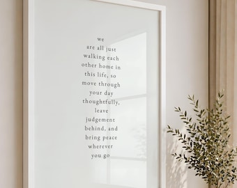 May include: A rectangular wall art piece in a white frame featuring black text on a white background that reads: we are all just walking each other home in this life, so move through your day thoughtfully, leave judgement behind, and bring peace wherever you go.