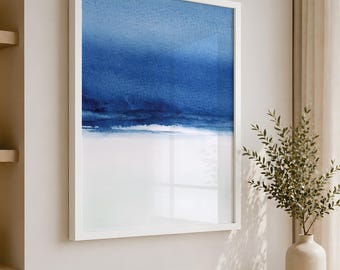 May include: A framed vertical wall art piece featuring an abstract watercolor painting with a deep blue upper section that transitions into a lighter blue and white horizon line, encased in a clean white frame hanging on a neutral wall.