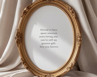 May include: An oval-shaped gold picture frame with ornate, decorative scrollwork detailing along the edges. The frame contains a white insert with black text that reads: blessed to have spent nineteen years loving you. you're still my greatest gift. love you forever.