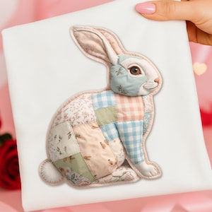 May include: A white fabric square with a patchwork bunny applique. The bunny has a white face, pink ears, and a body made of pastel-coloured fabric squares with floral and gingham patterns. The bunny is held by a hand.
