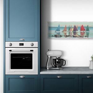K&ouml;nnte beinhalten: Eine wei&szlig;e K&uuml;che mit blauen Schr&auml;nken, einem wei&szlig;en Backofen und einer wei&szlig;en K&uuml;chenmaschine. Ein gerahmtes Bild von Segelbooten auf einem See h&auml;ngt an der Wand &uuml;ber der Arbeitsplatte.