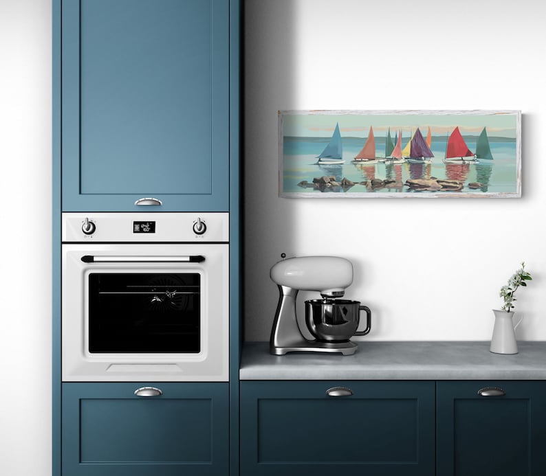 K&ouml;nnte beinhalten: Eine wei&szlig;e K&uuml;che mit blauen Schr&auml;nken, einem wei&szlig;en Backofen und einer wei&szlig;en K&uuml;chenmaschine. Ein gerahmtes Bild von Segelbooten auf einem See h&auml;ngt an der Wand &uuml;ber der Arbeitsplatte.