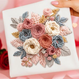 Op de afbeelding: Een wit vierkant canvas met een gedetailleerd bloemenborduurontwerp. De borduursels gebruiken verschillende garenkleuren, zoals roze, blauw, crème en goud, waardoor een gestructureerd, driedimensionaal effect ontstaat. De bloemen en bladeren zijn ingewikkeld geborduurd.