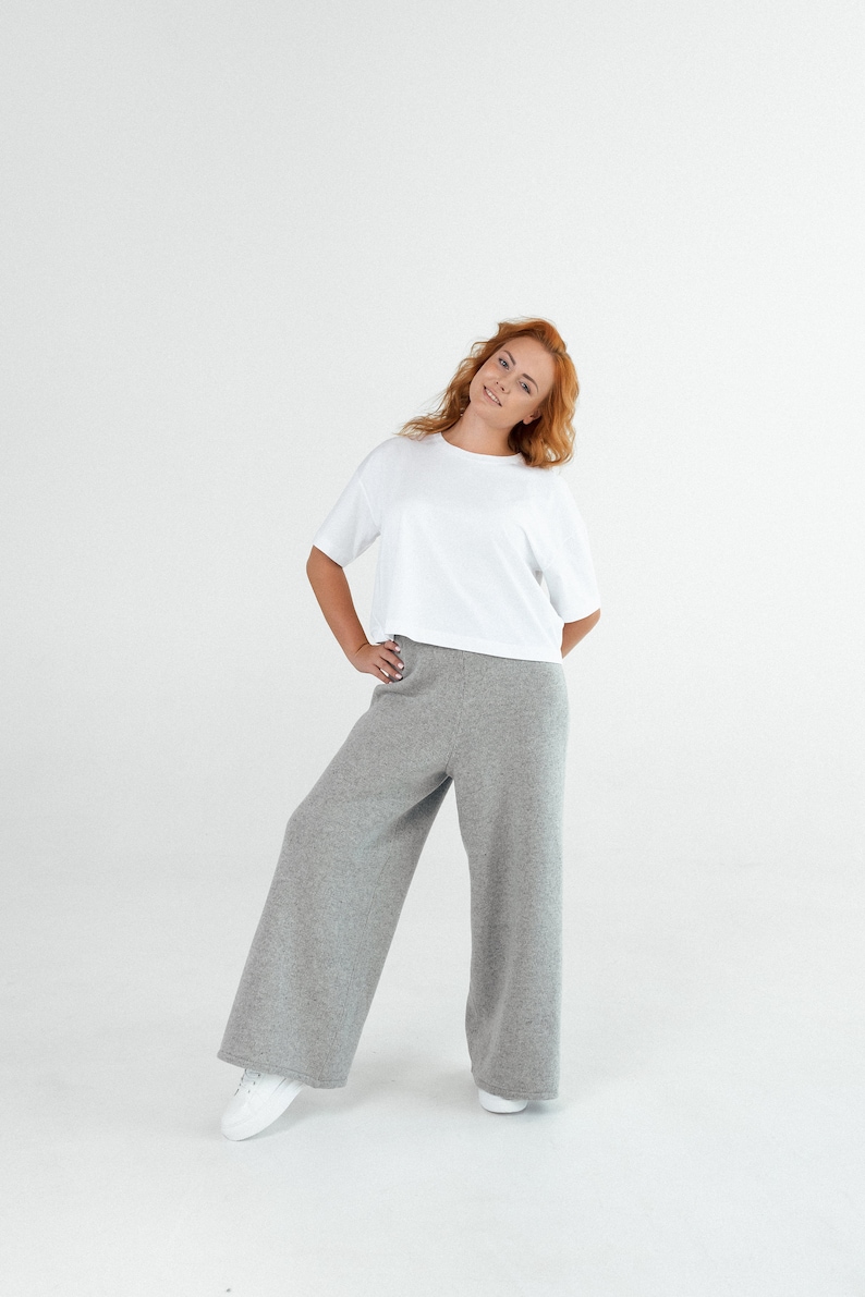 May include: A woman wearing a white t-shirt and gray wide-leg pants. She is standing on a white background.