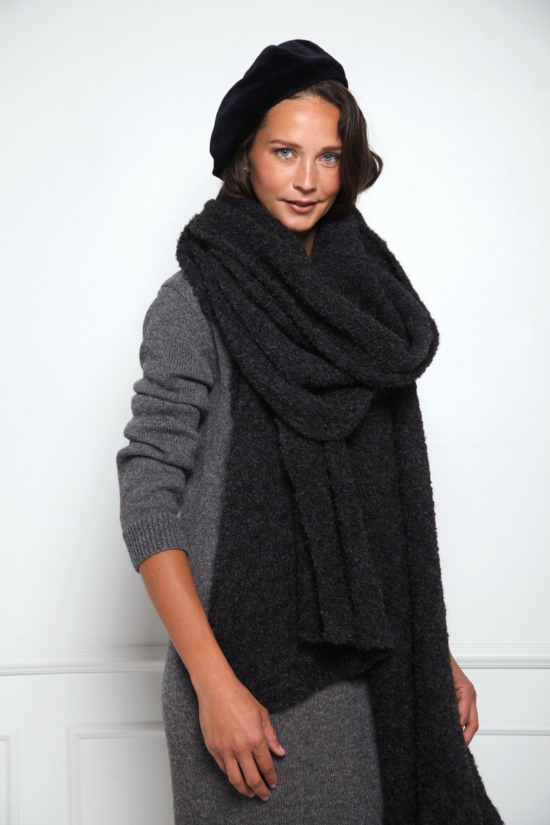 May include: A woman wearing a gray sweater dress and a black beret, with a thick, dark gray fuzzy scarf wrapped around her neck.