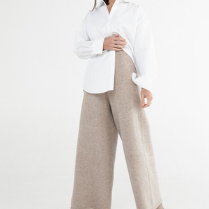 May include: A woman wearing a white button-down shirt and wide-leg, beige knit pants. She is wearing beige heeled boots.
