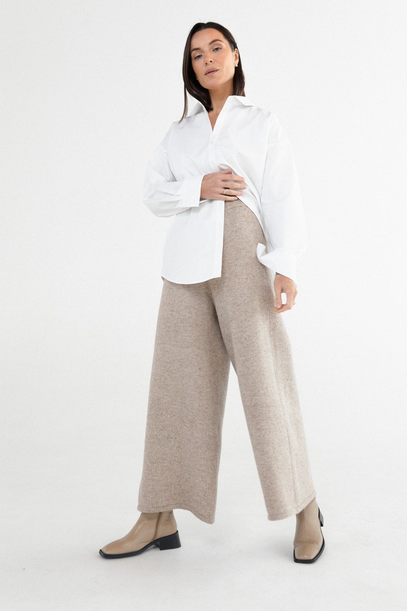 May include: A woman wearing a white button-down shirt and wide-leg, beige knit pants. She is wearing beige heeled boots.