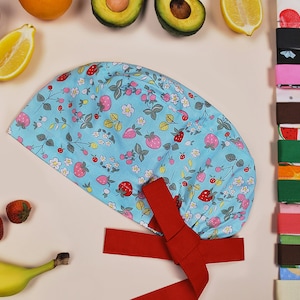 Puede incluir: Un gorro de quirófano azul y blanco con estampado de fresas y flores, con un lazo rojo.
