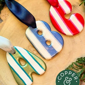 May include: Three letter-shaped ornaments labeled A, B, and C. The A is green and white, the B is blue and white, and the C is red and white. Each ornament features a satin ribbon loop for hanging and a glossy finish. A logo reads COPPER & GREEN.