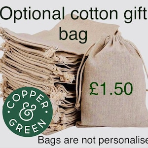 May include: A stack of light beige cotton drawstring gift bags with a textured weave. One bag stands upright in the foreground. The text reads Optional cotton gift bag, &pound;1.50, and Bags are not personalised, with a circular Copper & Green logo.