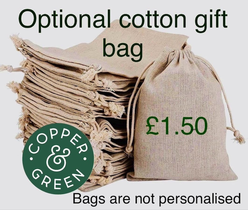 May include: A stack of light beige cotton drawstring gift bags with a textured weave. One bag stands upright in the foreground. The text reads Optional cotton gift bag, &pound;1.50, and Bags are not personalised, with a circular Copper & Green logo.