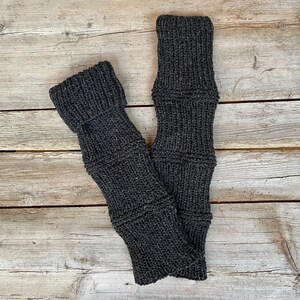 Könnte beinhalten: Ein Paar graue gestrickte Beinstulpen mit gerippter Struktur. Die Beinstulpen sind in der Mitte gefaltet und auf einer Holzoberfläche abgelegt.