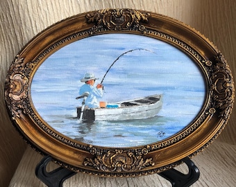 May include: An oval oil painting in an ornate gold frame depicting a person in a light blue shirt and white hat fishing from a small white boat on calm blue water. The scene shows a fishing rod bent with a line cast into the water.