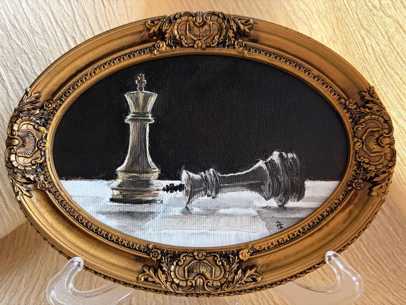 May include: An oval oil painting in a decorative gold frame featuring a standing white chess king and a fallen black chess king on a white surface against a black background. The painting captures the contrast between the two pieces in detail.