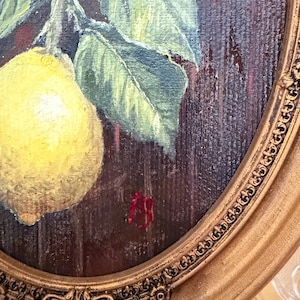 Pode incluir: Uma pintura a &oacute;leo numa moldura oval representando um lim&atilde;o amarelo com folhas verdes sobre um fundo de madeira castanho escuro. A pintura apresenta pinceladas vis&iacute;veis e uma assinatura vermelha perto do centro inferior da tela.