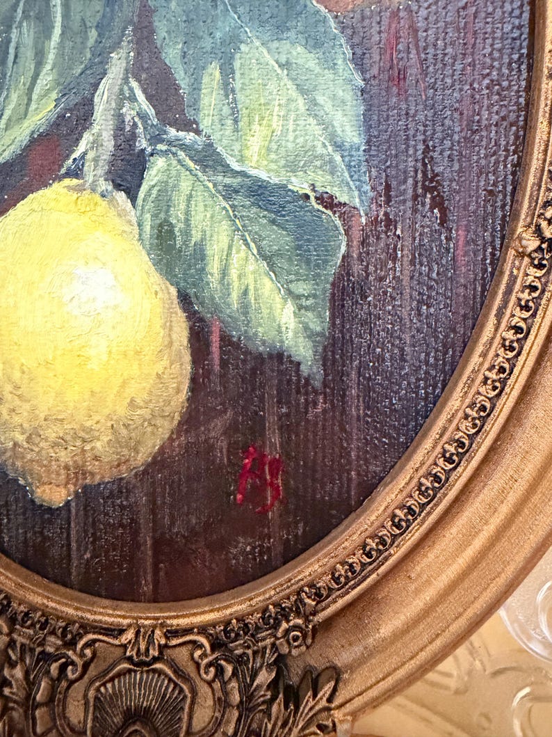 Pode incluir: Uma pintura a &oacute;leo numa moldura oval representando um lim&atilde;o amarelo com folhas verdes sobre um fundo de madeira castanho escuro. A pintura apresenta pinceladas vis&iacute;veis e uma assinatura vermelha perto do centro inferior da tela.
