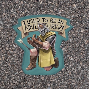 Puede incluir: Una pegatina con una ilustración de dibujos animados de un aventurero herido con una flecha en la pierna. La pegatina tiene un fondo azul y el texto "¡Yo era un aventurero!" en una pancarta.