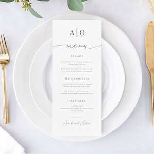 Peut inclure: Un menu de mariage blanc avec les noms du couple, Amanda et Oliver, en bas. Le menu liste les différents plats : Salades, Plats principaux et Desserts. Le menu est imprimé sur un papier texturé.