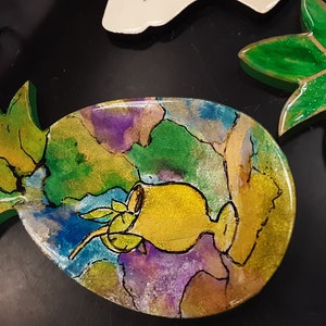 Könnte beinhalten: Eine grüne und gelbe Ananas-förmige Schale mit einem bemalten Design eines tropischen Getränks mit einem Strohhalm und einer Limettenscheibe. Die Schale ist aus Harz und hat eine glänzende Oberfläche.