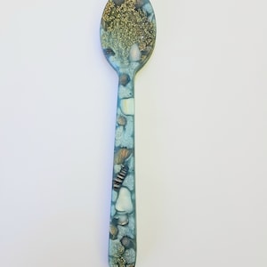 May include: A blue spoon with gold glitter and seashells embedded in the resin. The spoon is a unique and decorative piece.