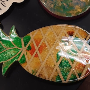 Könnte beinhalten: Ein Ananas-Untersetzer aus Harz mit grünem Oberteil und gelbem Körper mit einem goldenen und grünen Rautenmuster.