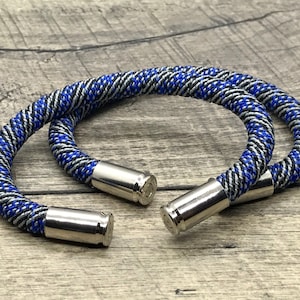 May include: Two blue, black, and silver braided bracelets with bullet casings as clasps.