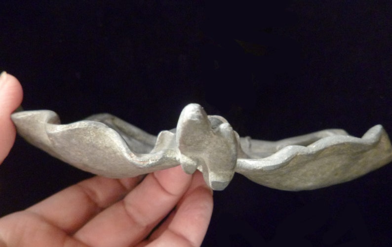 May include: A silver-colored metal dish with a wavy, organic shape. The dish is designed to resemble a leaf or flower.