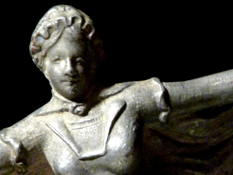 May include: A silver statue of a woman with her arms outstretched. She is wearing a long, flowing robe with a high collar.