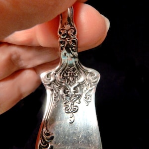 May include: Close-up of the ornate, silver handle of a butter knife. The handle is decorated with intricate floral designs.