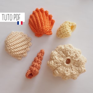 May include: Five crocheted seashells in orange and cream colours. The shells are arranged on a white surface. The text "TUTO PDF" is in the top left corner of the image.