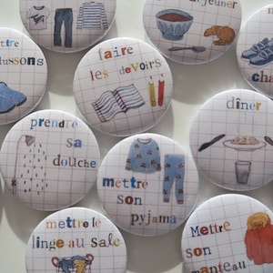 May include: Nine colourful round buttons with illustrations and French text. The buttons feature activities like taking a shower, getting dressed, eating dinner, and doing homework.