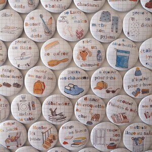 May include: A collection of colourful round buttons with illustrations and French text. The buttons feature various activities like taking a bath, putting on pyjamas, brushing teeth, and getting dressed.
