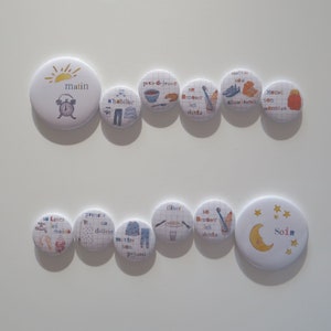 May include: A set of 12 colourful round buttons with illustrations and text in French. The buttons depict a daily routine for children, including getting dressed, brushing teeth, eating breakfast, and going to bed. The buttons are perfect for teaching children about daily routines and can be used as a visual aid for parents and teachers.