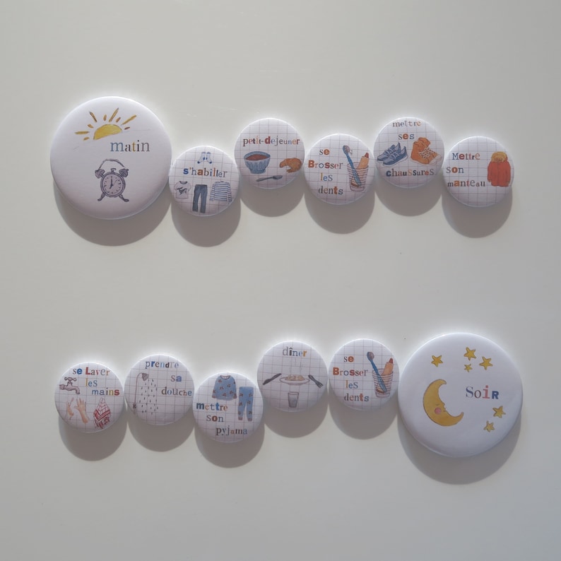 May include: A set of 12 colourful round buttons with illustrations and text in French. The buttons depict a daily routine for children, including getting dressed, brushing teeth, eating breakfast, and going to bed. The buttons are perfect for teaching children about daily routines and can be used as a visual aid for parents and teachers.