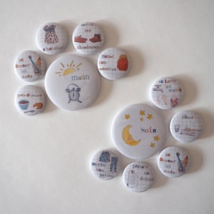 May include: Ten round white buttons with colourful illustrations and text in French. The buttons depict daily routines, such as getting dressed, brushing teeth, eating breakfast, and going to bed.