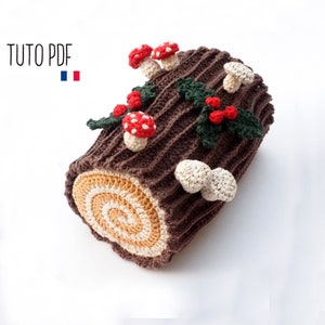 Op de afbeelding: Een gehaakte kerstboomstam met bruine, witte en rode accenten. De stam is versierd met hulstbladeren en rode bessen, en gekroond met paddenstoelen.