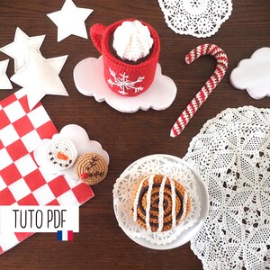 Peut inclure: Des articles de Noël en crochet, dont une tasse rouge avec de la crème fouettée blanche, une canne en sucre, un bonhomme de neige, un bonhomme en pain d'épices et un pain à la cannelle. Les articles sont disposés sur une surface en bois avec des napperons blancs et une nappe à carreaux rouge et blanc. Le texte "TUTO PDF" est visible dans le coin inférieur gauche de l'image.