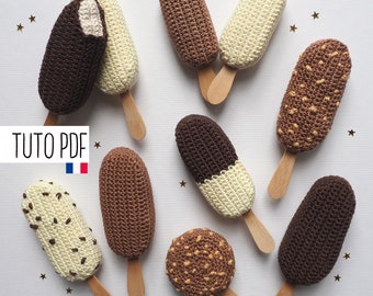 May include: A collection of handmade crochet ice cream popsicles in various colors and textures. The popsicles include chocolate, vanilla, and nut-covered designs, each with a wooden stick. The image includes the text "TUTO PDF" and the French flag.