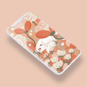 Pu&ograve; includere: Una custodia per telefono bianca con un design floreale che presenta una volpe bianca che dorme in un letto di fiori arancioni e bianchi. Lo sfondo &egrave; di colore pesca chiaro.
