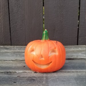 May include: A small orange pumpkin with a carved jack-o'-lantern face. The pumpkin is sitting on a wooden surface.